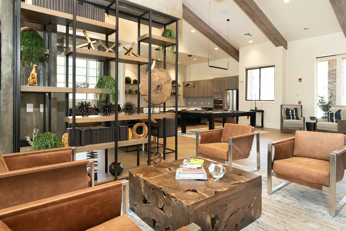 This scene presents a tastefully decorated living area with shelves of decorative items, a wooden coffee table, leather chairs, and an open kitchen. The setting looks modern, comfortable, and ready for both casual relaxation and social gatherings.
