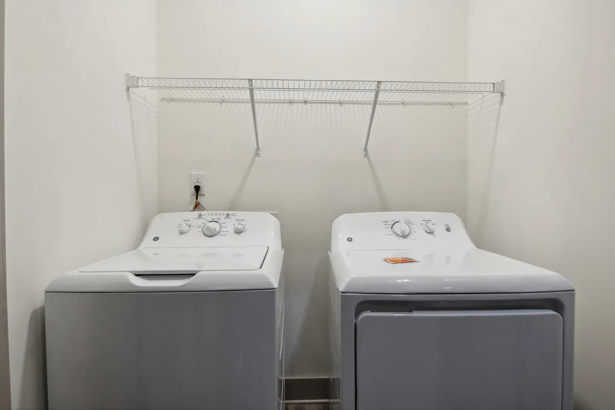 A tidy laundry area featuring a modern washing machine, dryer, and organized shelving for supplies. The space is functional and ready for use, making daily chores effortless.