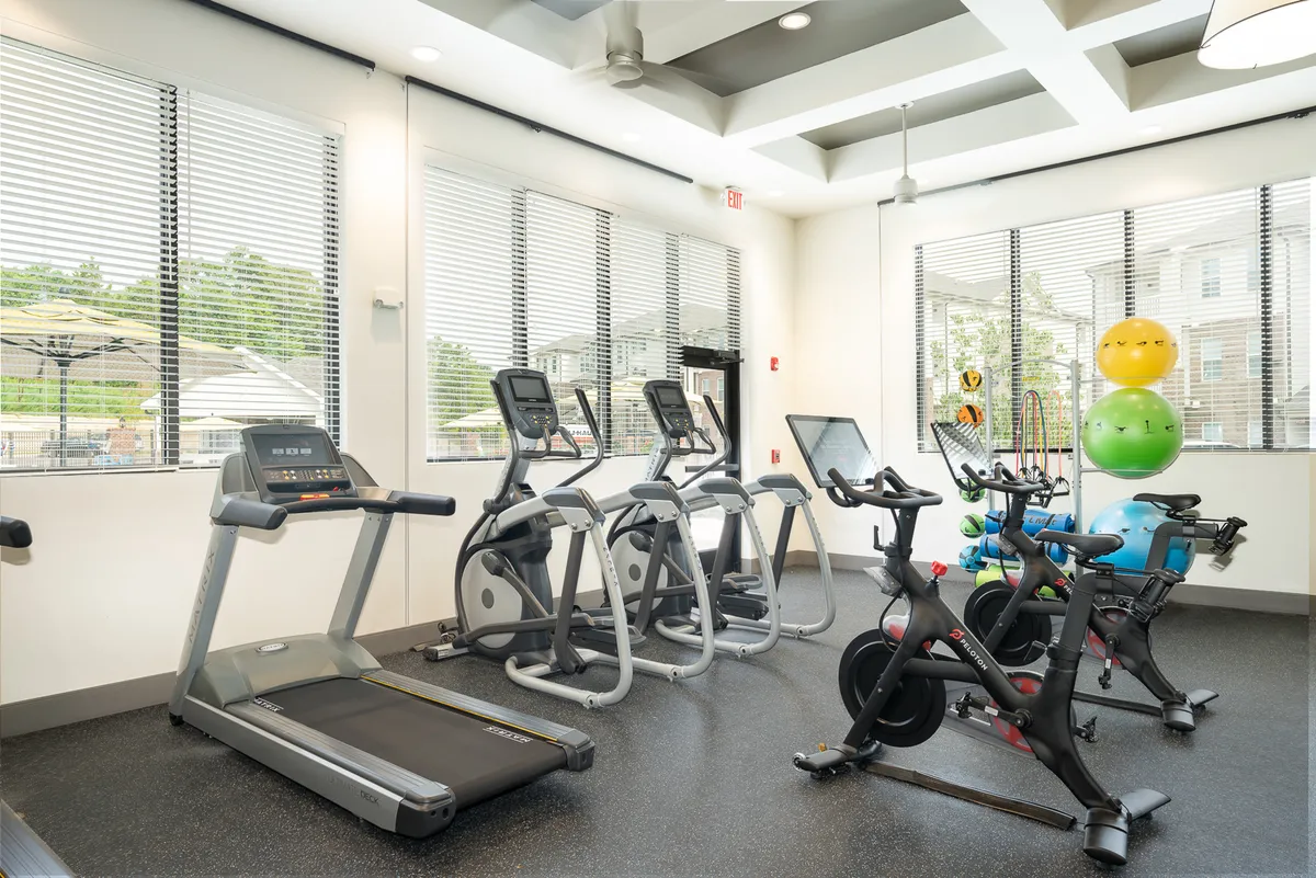 A well-equipped fitness center filled with treadmills, elliptical machines, stationary bikes, and exercise balls. Natural light fills the room, and there is ample space for both individual workouts and group fitness classes.
