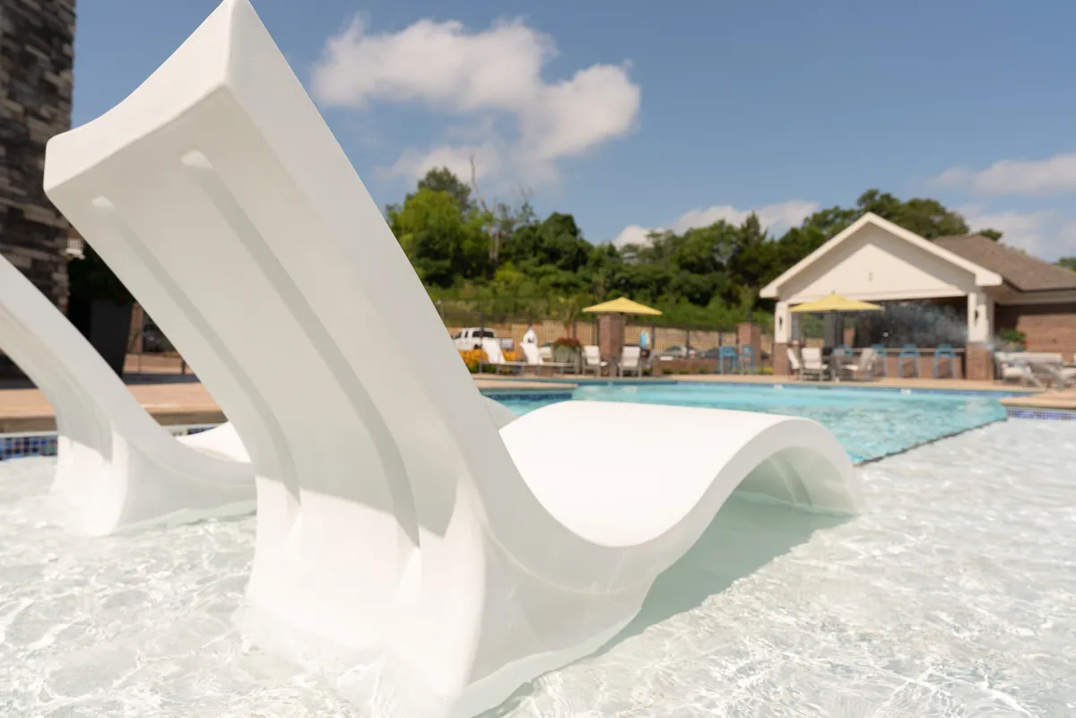 A tranquil swimming pool surrounded by lounge chairs and lush greenery. The setting invites residents to sunbathe, swim, or socialize by the water, capturing the essence of leisure and relaxation.