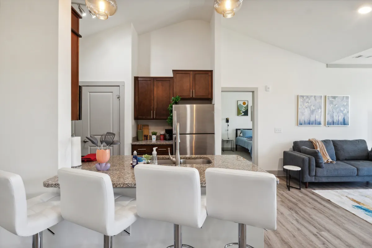 A contemporary kitchen space featuring a prominent kitchen island, sleek stainless steel appliances, and a comfortable sofa visible in the background. Artwork adds a touch of personality, while the open layout hints at both cooking and entertaining possibilities. The space is well-lit, with surfaces that showcase the stone countertops and modern design aesthetic.