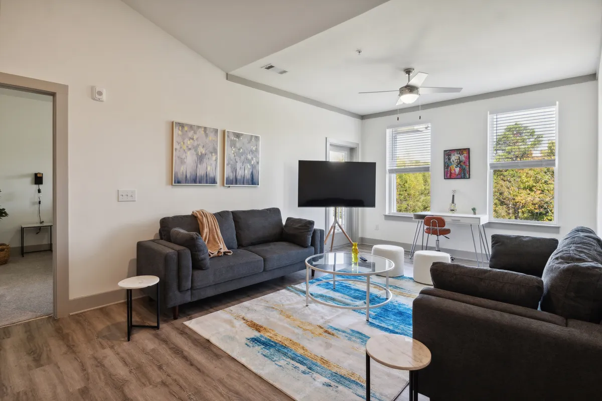 The image showcases a sunlit, stylish living area featuring comfortable sofas arranged around a sleek coffee table. Modern artwork adds personality to the space, while large windows bathe the room in natural light and offer inviting views. The overall atmosphere is one of cozy sophistication, perfect for relaxing afternoons or intimate evening gatherings.