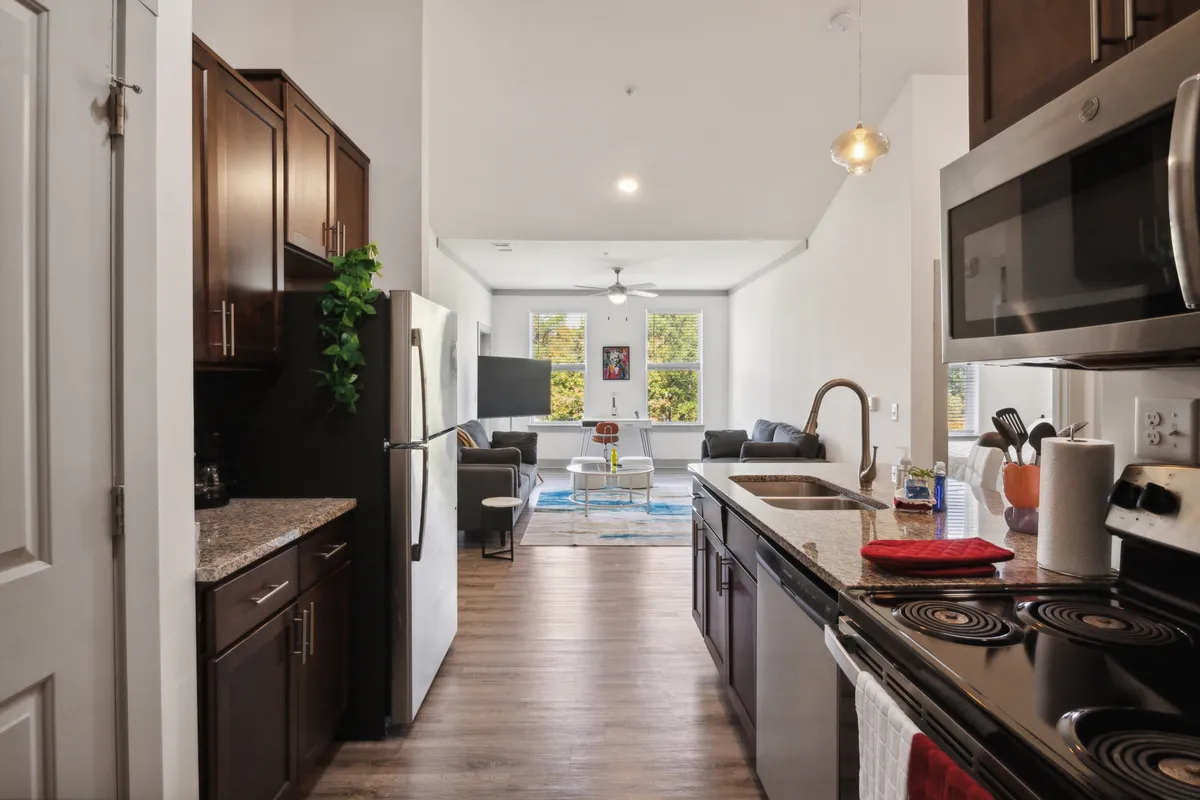 A modern open-plan living space featuring a granite countertop, stainless steel appliances, large windows, and inviting decorative wall art. The area blends kitchen, dining, and relaxation zones, fostering productivity, entertainment, and comfortable day-to-day living.